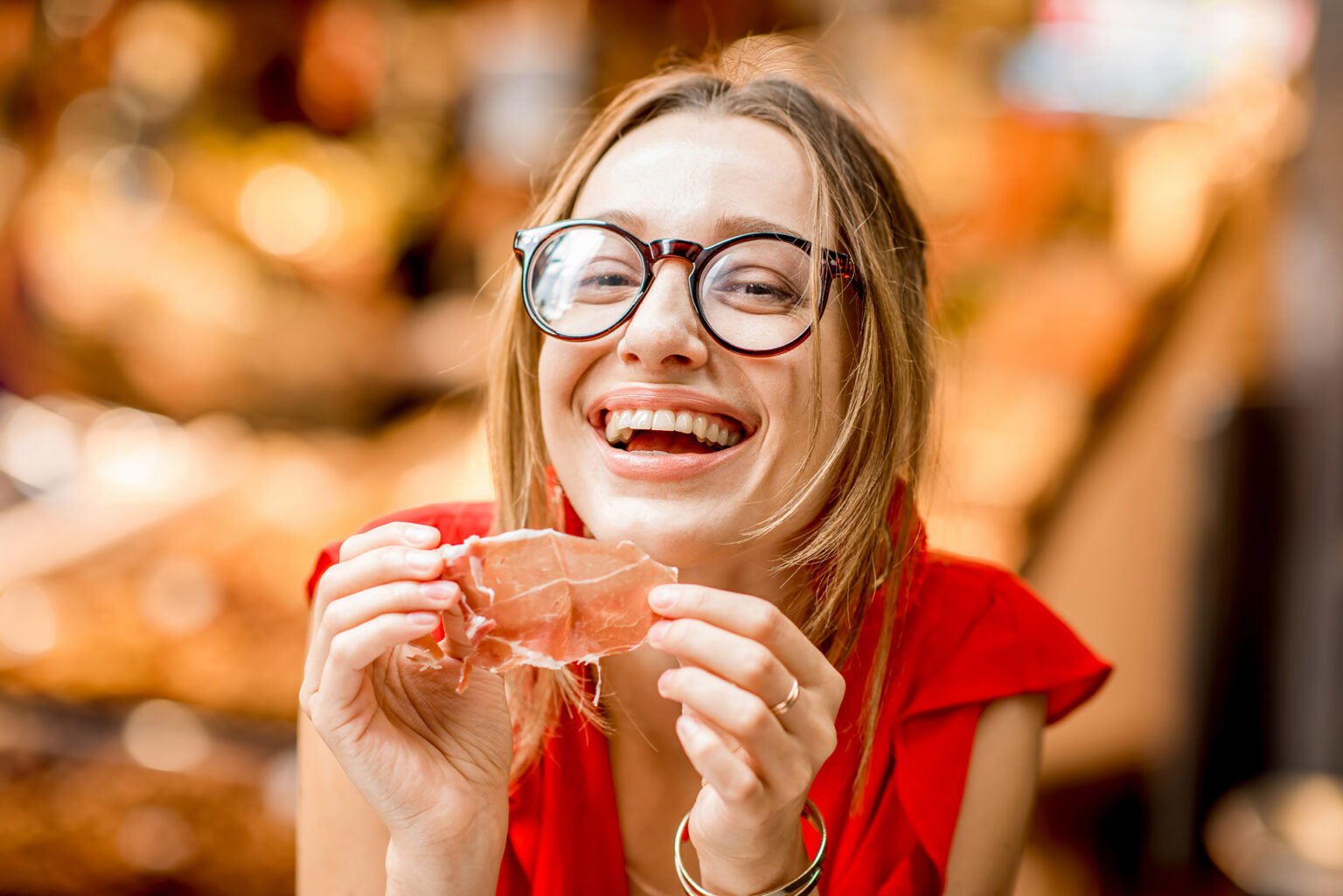 Young woman in red dress eating jamon traditional spanish dry-cured ham sitting at the Barcelona food market